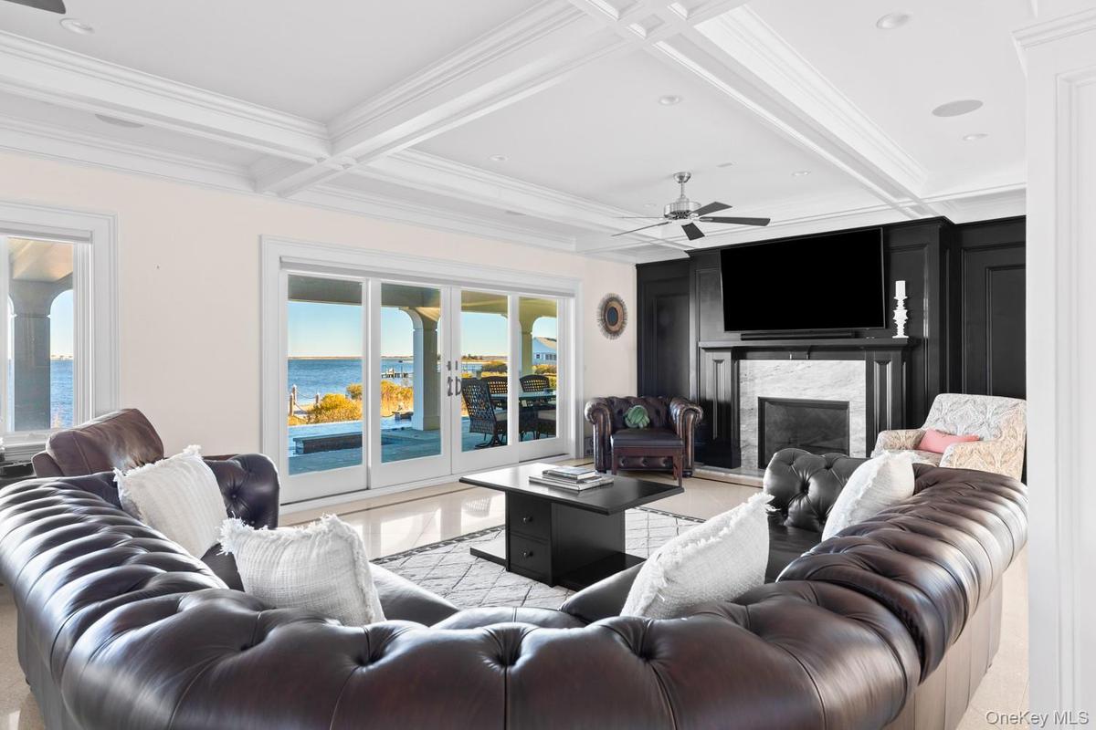 Living area with crown molding, coffered ceiling, a high end fireplace, beam ceiling, and ceiling fan