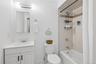 Bathroom featuring a white vanity with integrated sink, coordinating white toilet, and a tiled shower/tub combination with a decorative accent band