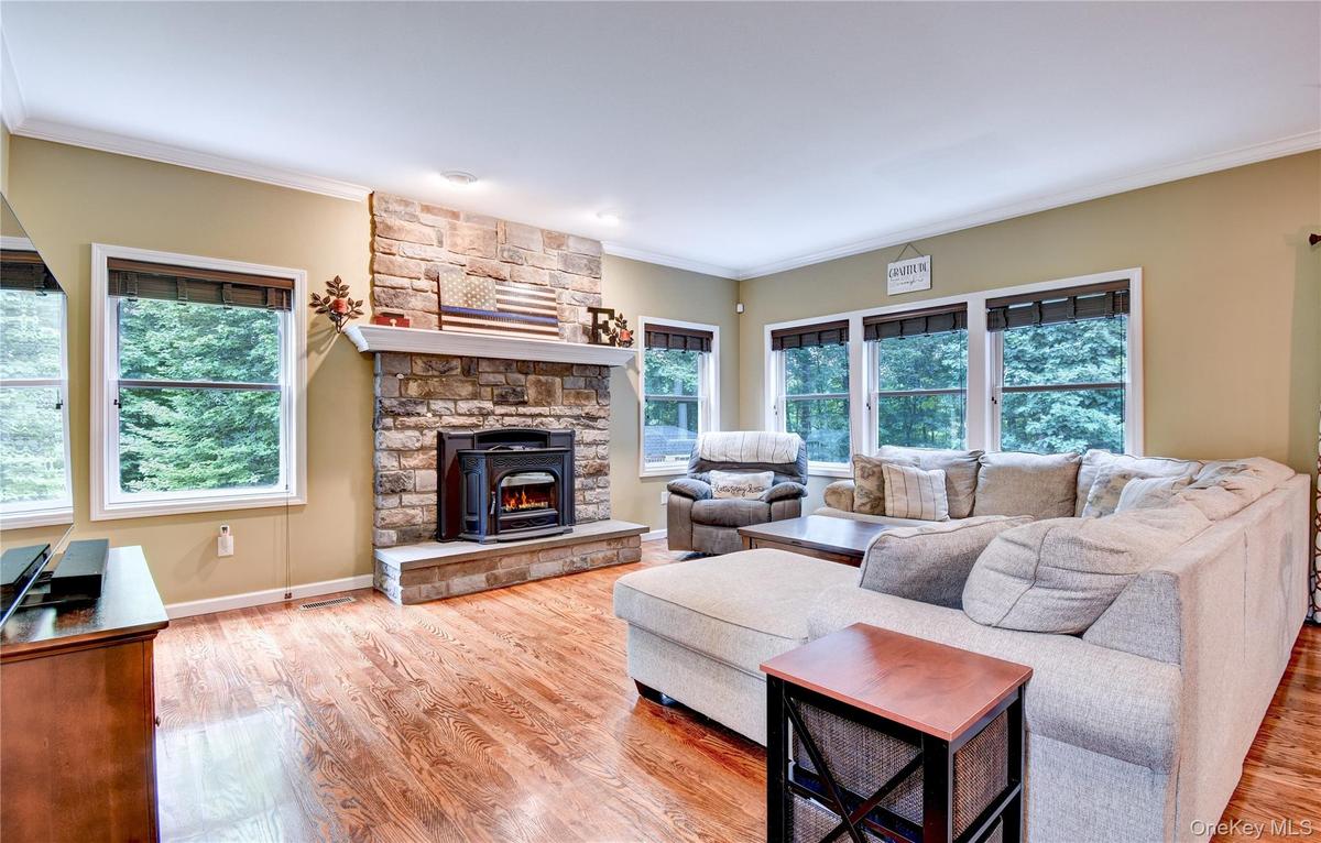 Living area featuring wood flooring, a stone-faced fireplace with hearth and pellet stove, recessed lighting, and multiple windows
