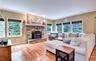 Living area featuring wood flooring, a stone-faced fireplace with hearth and pellet stove, recessed lighting, and multiple windows