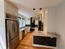 Well-appointed kitchen featuring light-toned cabinetry, stainless steel appliances, granite countertops, and hardwood flooring