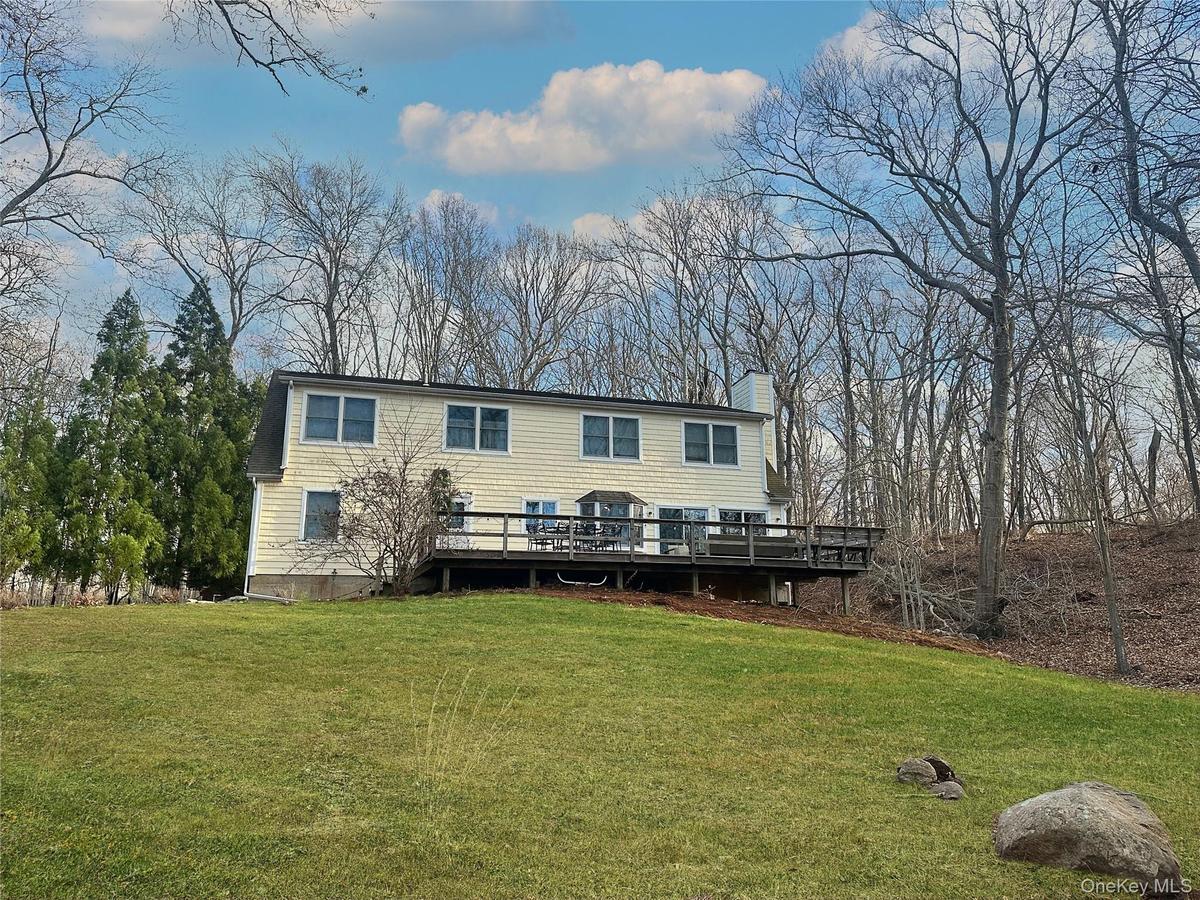 Rear view of house featuring a deck, a yard, a chimney, and view of wooded area