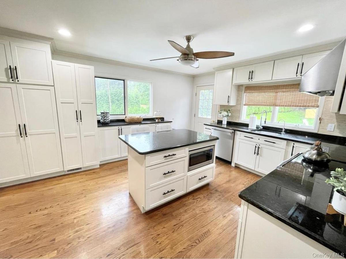 Kitchen with light wood-style floors, crown molding, ceiling fan, white cabinetry, and dark stone counters