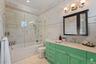 Bathroom featuring a single vanity with a pale countertop and a green base, tiled flooring, a built-in tub with a glass enclosure, a toilet, and a med