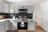 Kitchen with gray cabinetry, stainless steel appliances, backsplash, light wood finished floors, and light stone countertops
