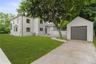 Contemporary white stucco exterior with black-framed windows, a detached single-car garage, mature landscaping, and an expansive lawn