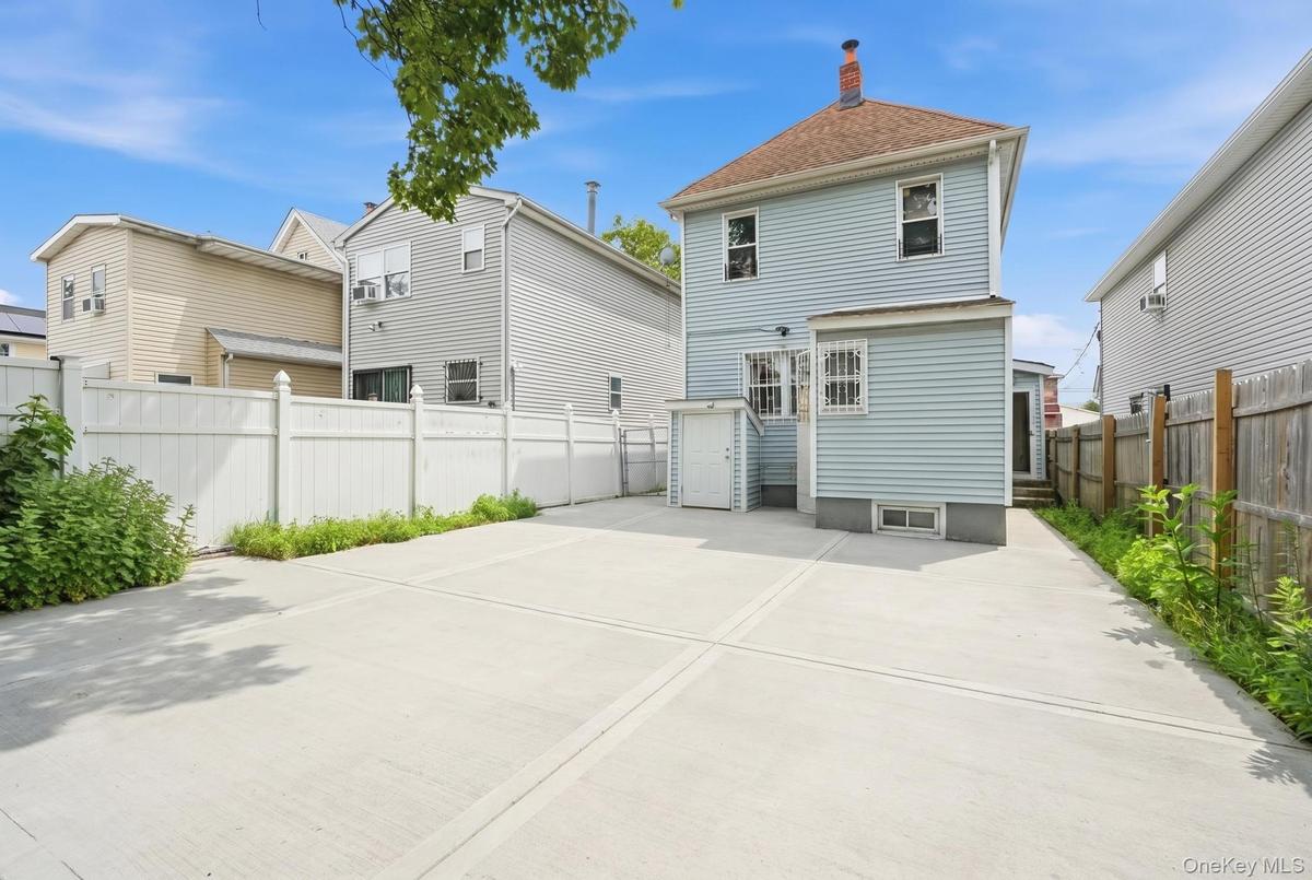 Spacious concrete paved yard featuring a white vinyl fence and a dedicated side entrance