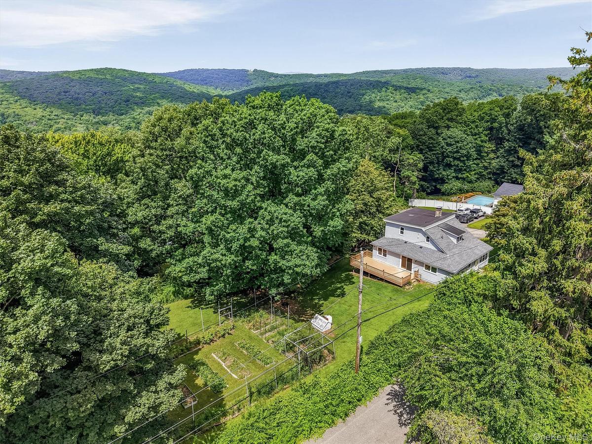 Home nestled among mature trees, featuring a light gray exterior, a multi-level roofline, and an expansive wooden deck