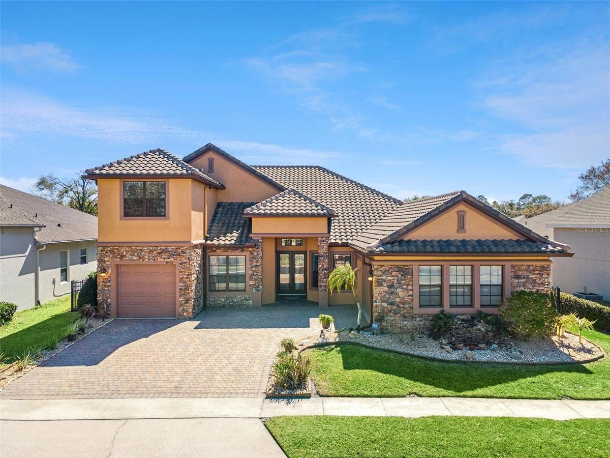 Elegant Sanford, FL home with striking stone façade, barrel tile roof, and an expansive paver driveway that enhances its upscale curb appeal.