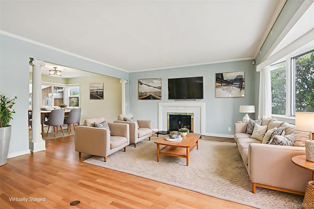 Living area featuring decorative columns, healthy amount of natural light, light wood-style flooring, crown molding, and a brick fireplace