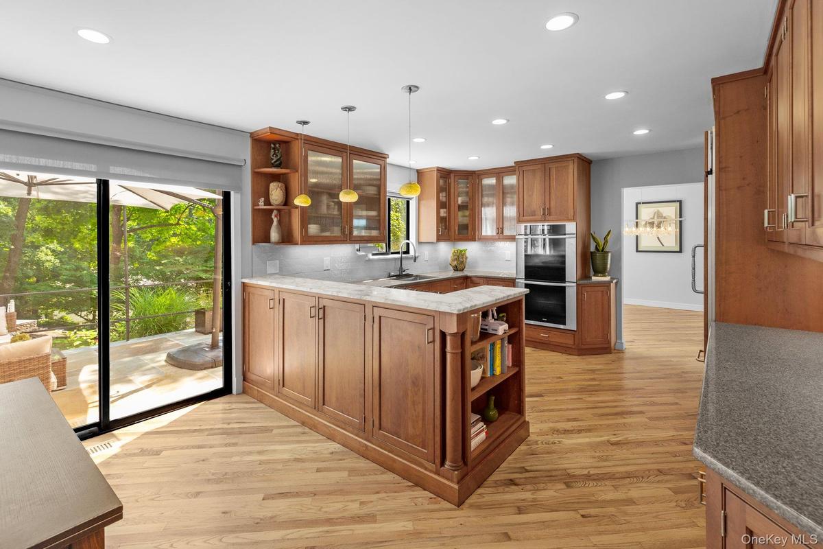 Kitchen featuring stainless steel double oven, brown cabinets, open shelves, and plenty of natural light