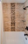 Tiled shower surround with decorative mosaic inlay, two recessed niches, and bronze fixtures