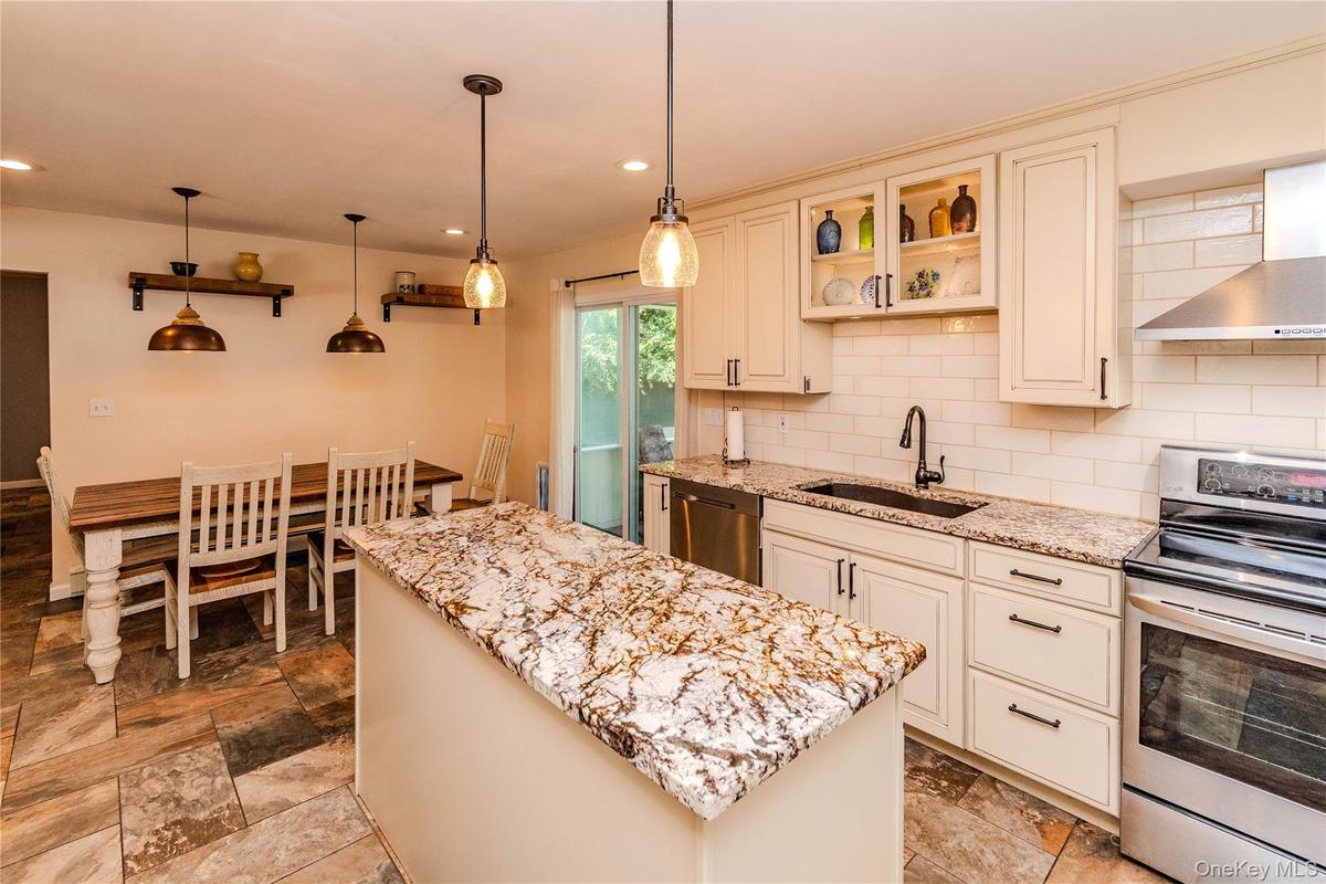 Kitchen featuring a central island with a stone countertop, stainless steel appliances, subway tile backsplash, and cream-colored cabinetry with displ