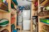 Utility closet featuring a stacked washer and dryer unit, water heater, and built-in shelving