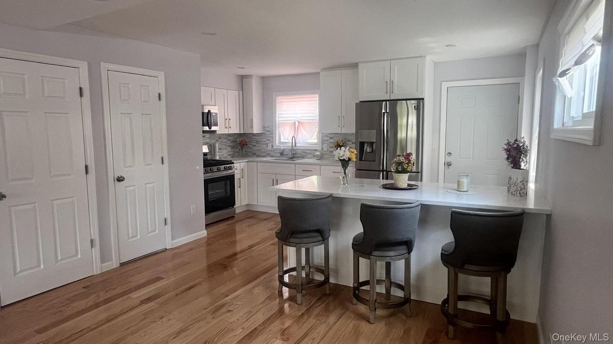 Open-concept kitchen featuring white shaker cabinetry, stainless steel appliances, a breakfast bar, countertops, and wood-finish flooring