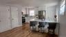 Open-concept kitchen featuring white shaker cabinetry, stainless steel appliances, a breakfast bar, countertops, and wood-finish flooring
