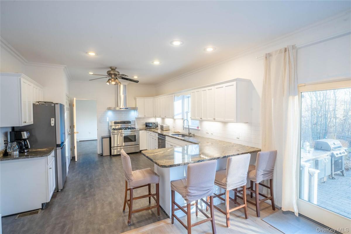Kitchen with stainless steel appliances, white cabinetry, a sink, a peninsula, and wall chimney exhaust hood