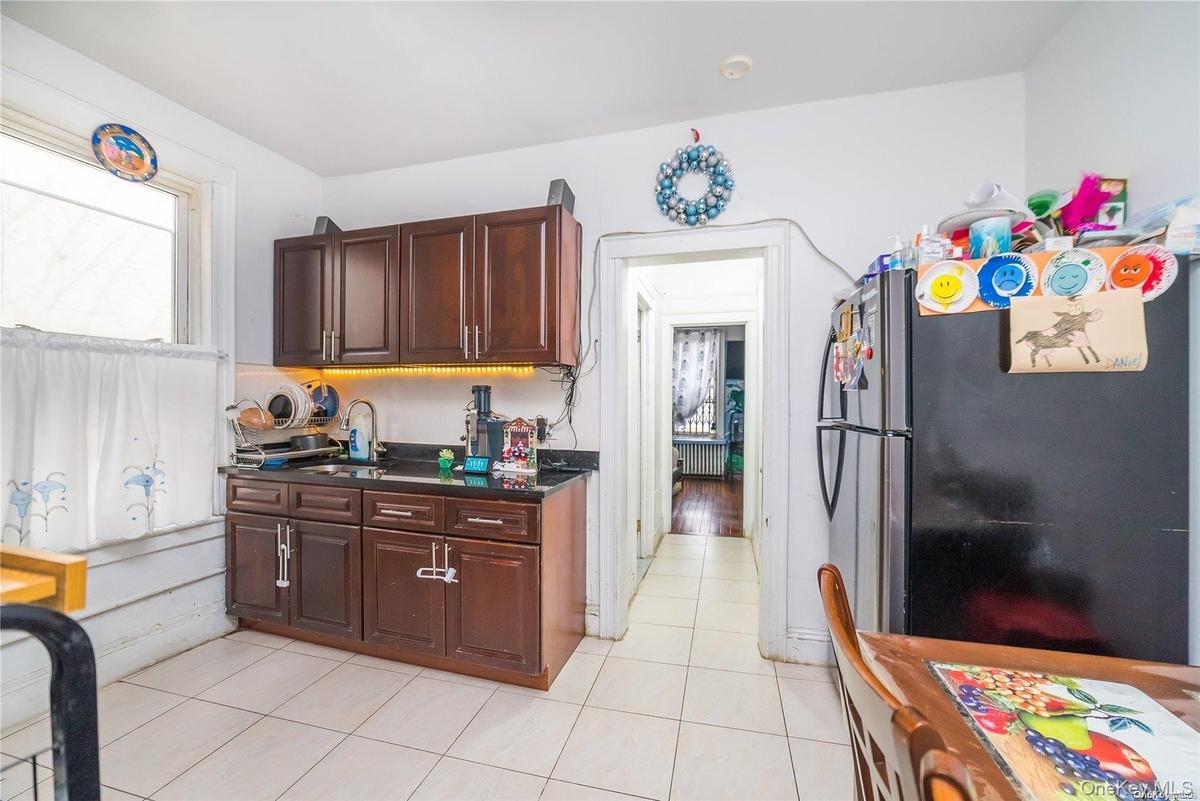 Kitchen featuring freestanding refrigerator, light tile patterned floors, dark brown cabinets, and dark stone counters