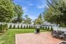 Expansive backyard featuring a brick paver patio, a manicured lawn, a white lattice fence, mature trees, and evergreen landscaping