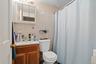 Bathroom featuring light-toned wall tile, a single vanity with wood-finish cabinetry, a mirrored medicine cabinet, and a shower area with a curtain ro