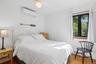 Bedroom featuring a ceiling fan, a wall-mounted air conditioning unit, a large window with black framing, and wood-finish flooring
