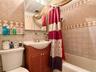 Bathroom featuring a tiled shower surround with decorative accent banding, a wood-finish vanity with an integrated sink, a wall-mounted mirror, and a 