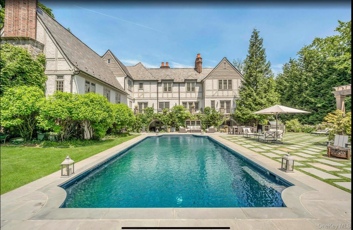This grand Tudor estate features a resort-caliber outdoor oasis centered around a sophisticated dark-bottom pool and a striking geometric stone terrac