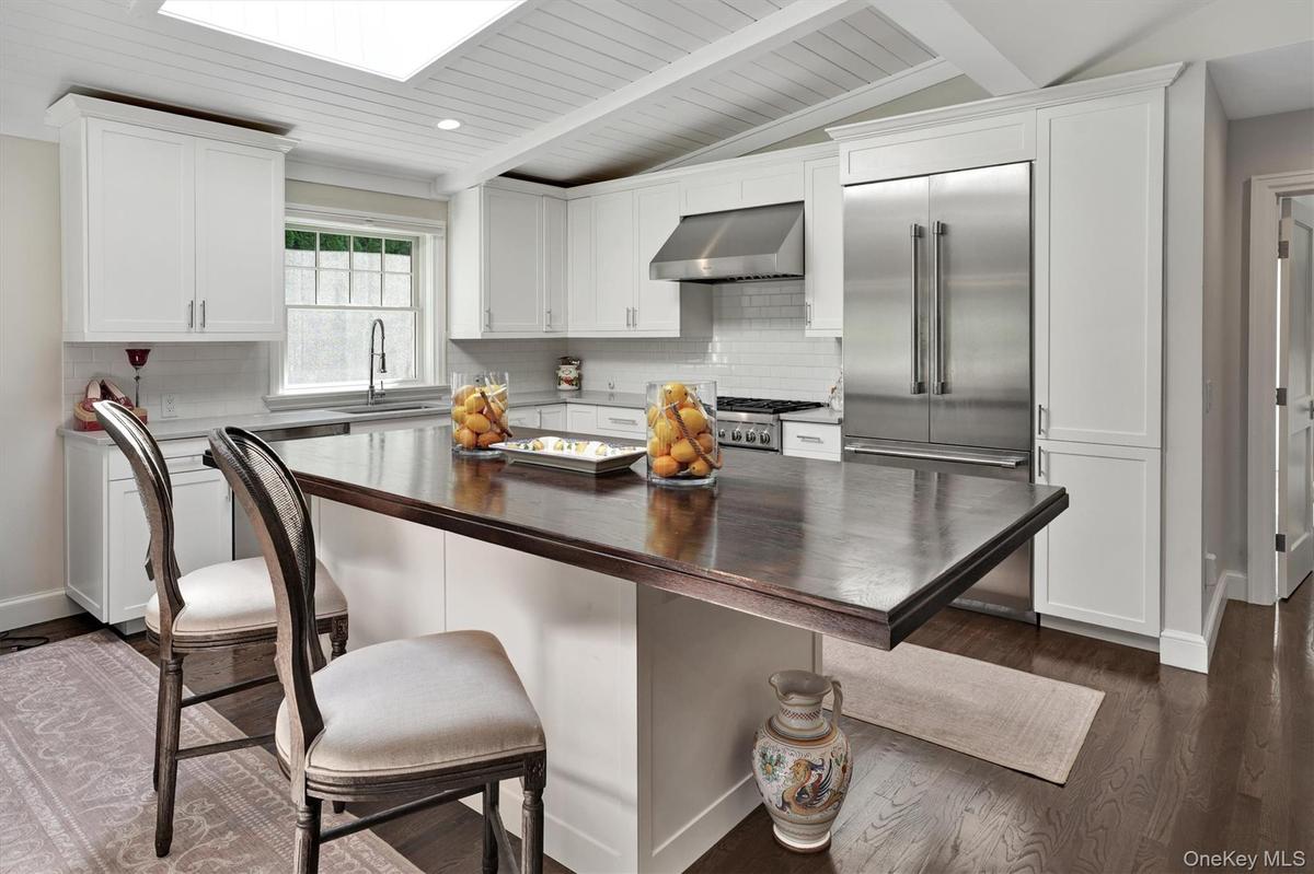 Kitchen featuring stainless steel built in fridge, dark wood finished floors, white cabinets, ventilation hood, and a breakfast bar area