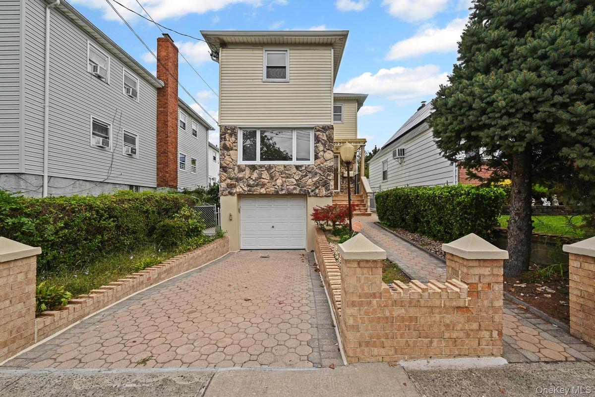 View of front facade with decorative driveway, stone siding, and an attached garage
