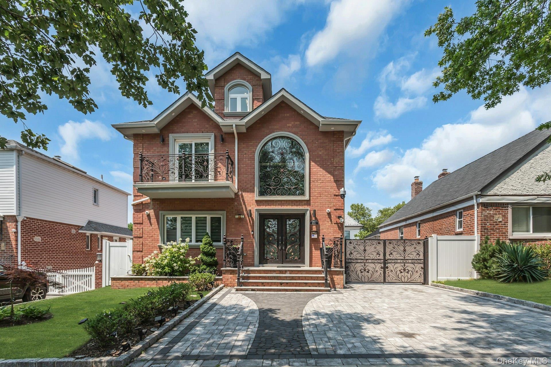 Brick face and side with a prominent elliptical window, double iron entry doors, and a second-story balcony with a decorative wrought iron railing
