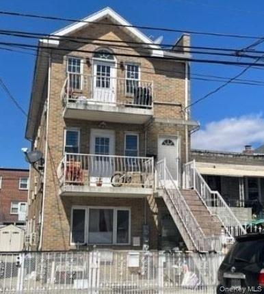 View of front facade featuring a balcony, a fenced front yard, and stairs