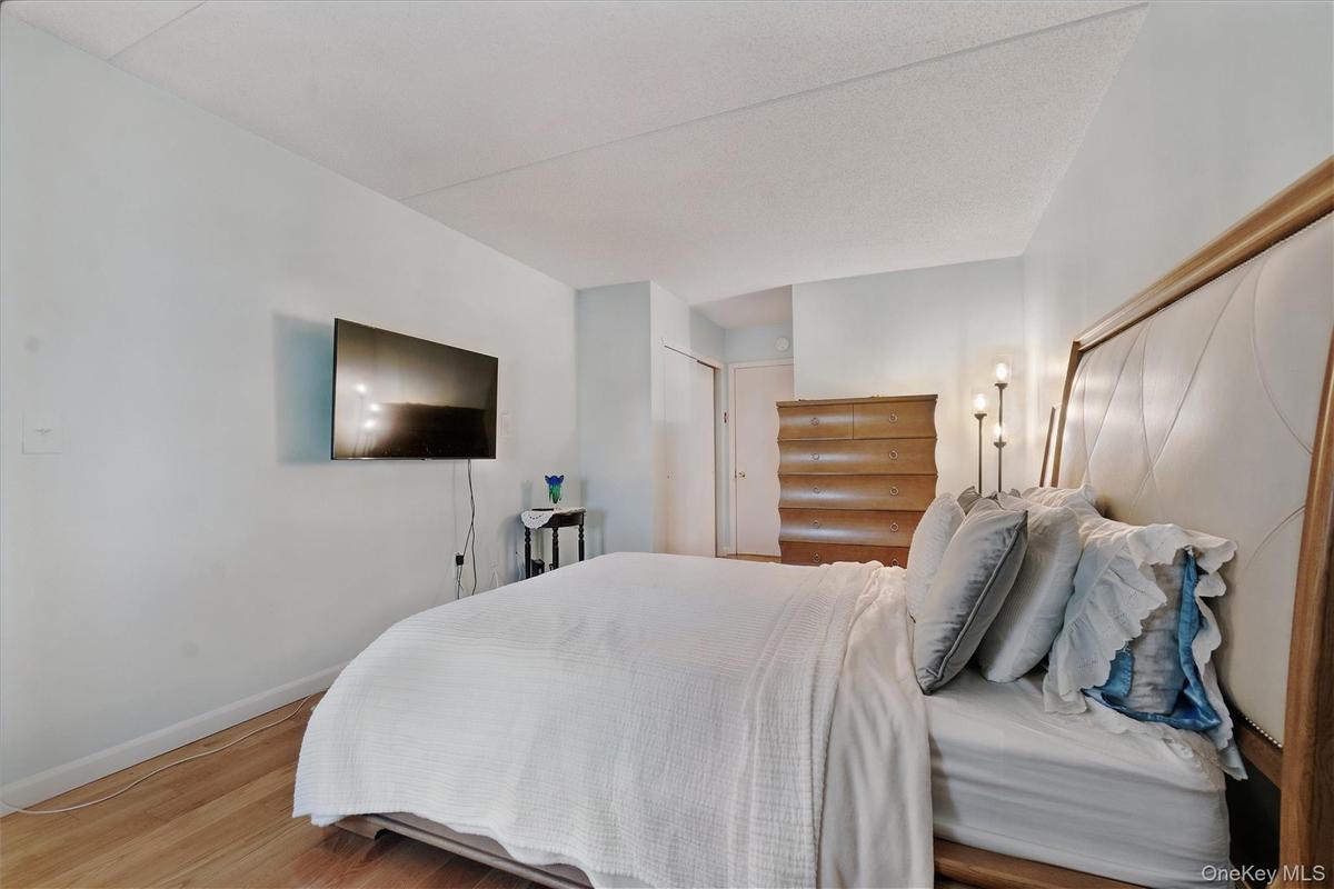 Bedroom featuring wood-finish flooring, a mounted television, a ceiling with textured finish, and light-colored wall paint