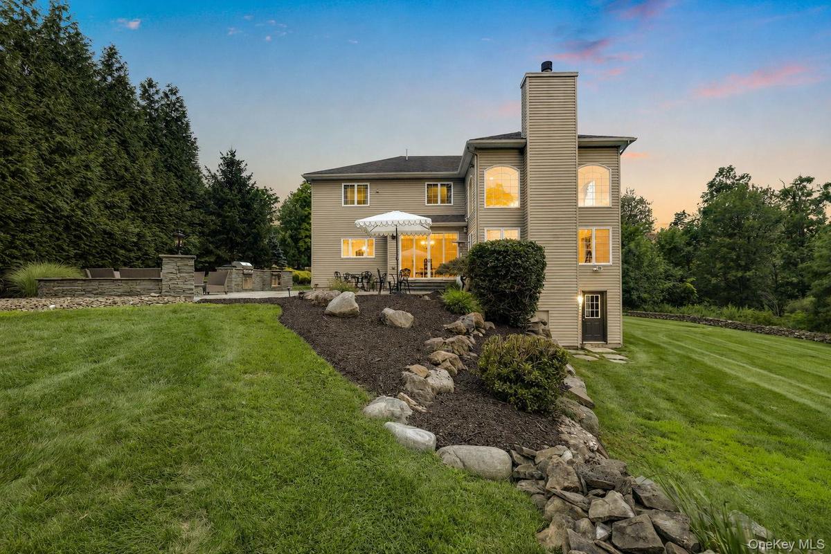 Rear exterior featuring multiple large windows, a stone-accented outdoor patio, and a dedicated outdoor cooking area