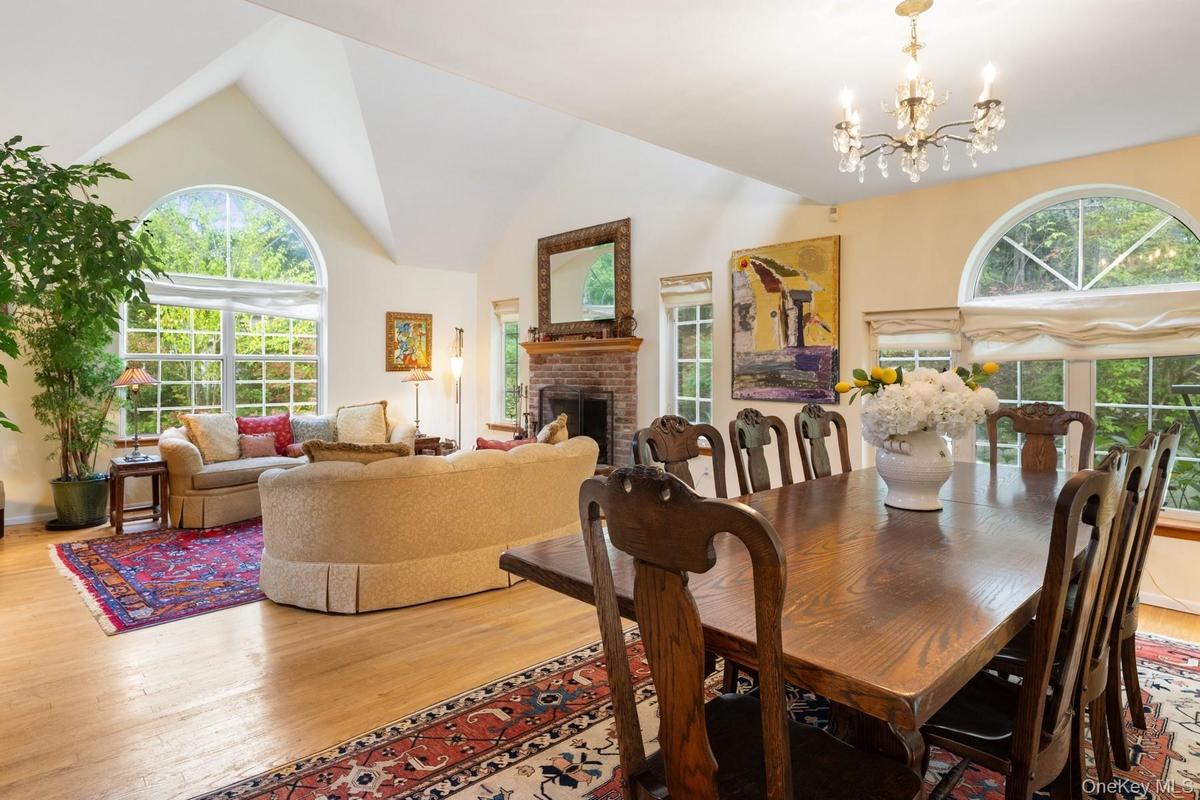 Dining room with a brick fireplace, light wood-type flooring, a chandelier, and high vaulted ceiling