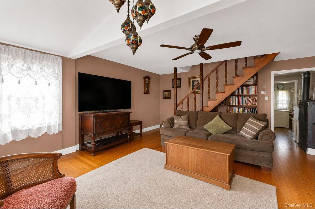 Living area featuring hardwood flooring, a built-in staircase with balusters, recessed built-in shelving, and a ceiling fan
