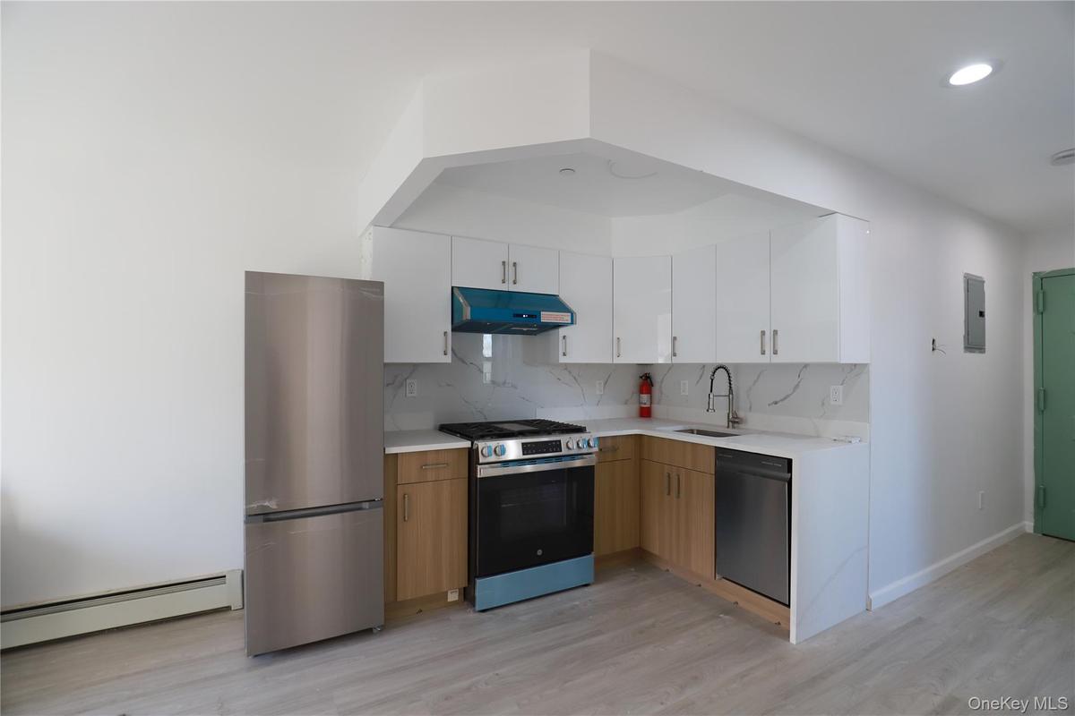 Kitchen featuring appliances with stainless steel finishes, backsplash, a baseboard heating unit, white cabinets, and light wood-type flooring
