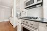 Stainless steel gas range with coordinating microwave and hood, complemented by a white subway tile backsplash, dark countertops, and white cabinetry