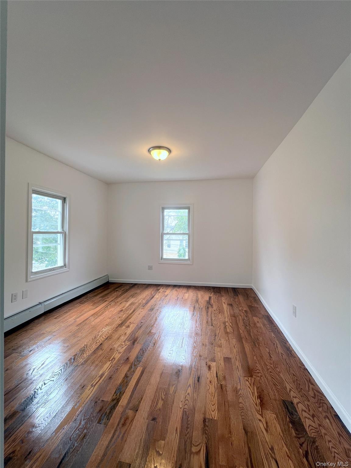 Spare room featuring a baseboard heating unit, plenty of natural light, and dark wood finished floors