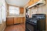 Kitchen featuring a black gas range, wood-finish flooring, light wood cabinetry, a stainless steel sink, and a range hood