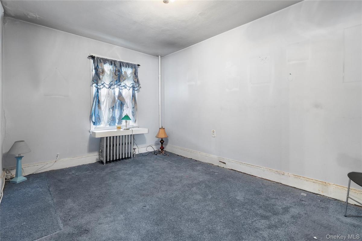 Carpeted spare room featuring radiator heating unit and baseboards