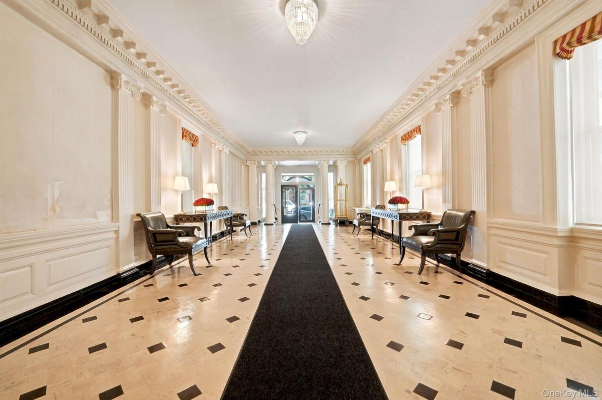 Hallway featuring stone tile flooring with contrasting accents, decorative wall paneling, and architectural columns