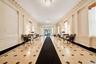 Hallway featuring stone tile flooring with contrasting accents, decorative wall paneling, and architectural columns