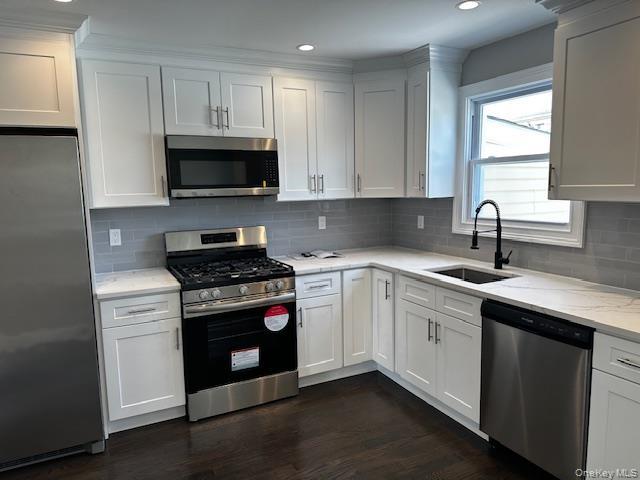 Kitchen with stainless steel appliances, dark wood-style flooring, recessed lighting, tasteful backsplash, and light stone countertops