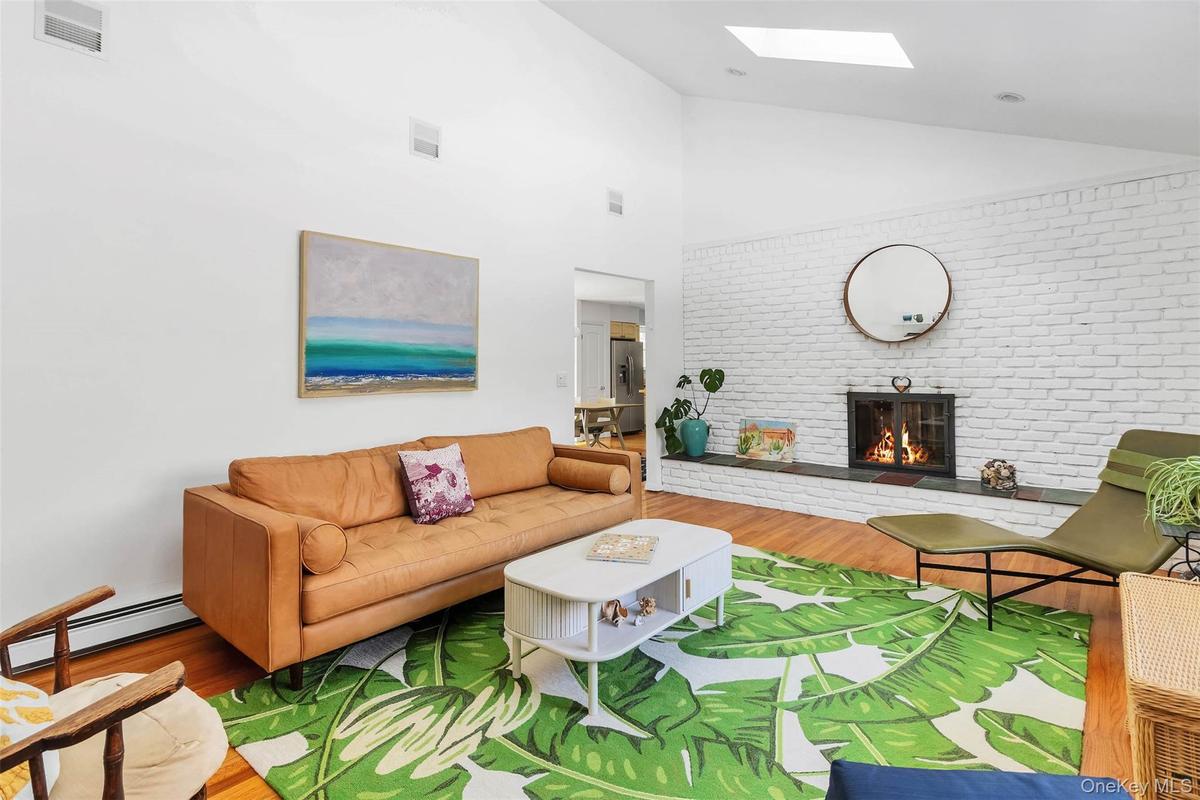 Living room with a baseboard heating unit, a skylight, a fireplace, wood-type flooring, and brick wall