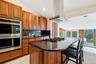 Kitchen featuring double oven, recessed lighting, island exhaust hood, brown cabinets, and vaulted ceiling