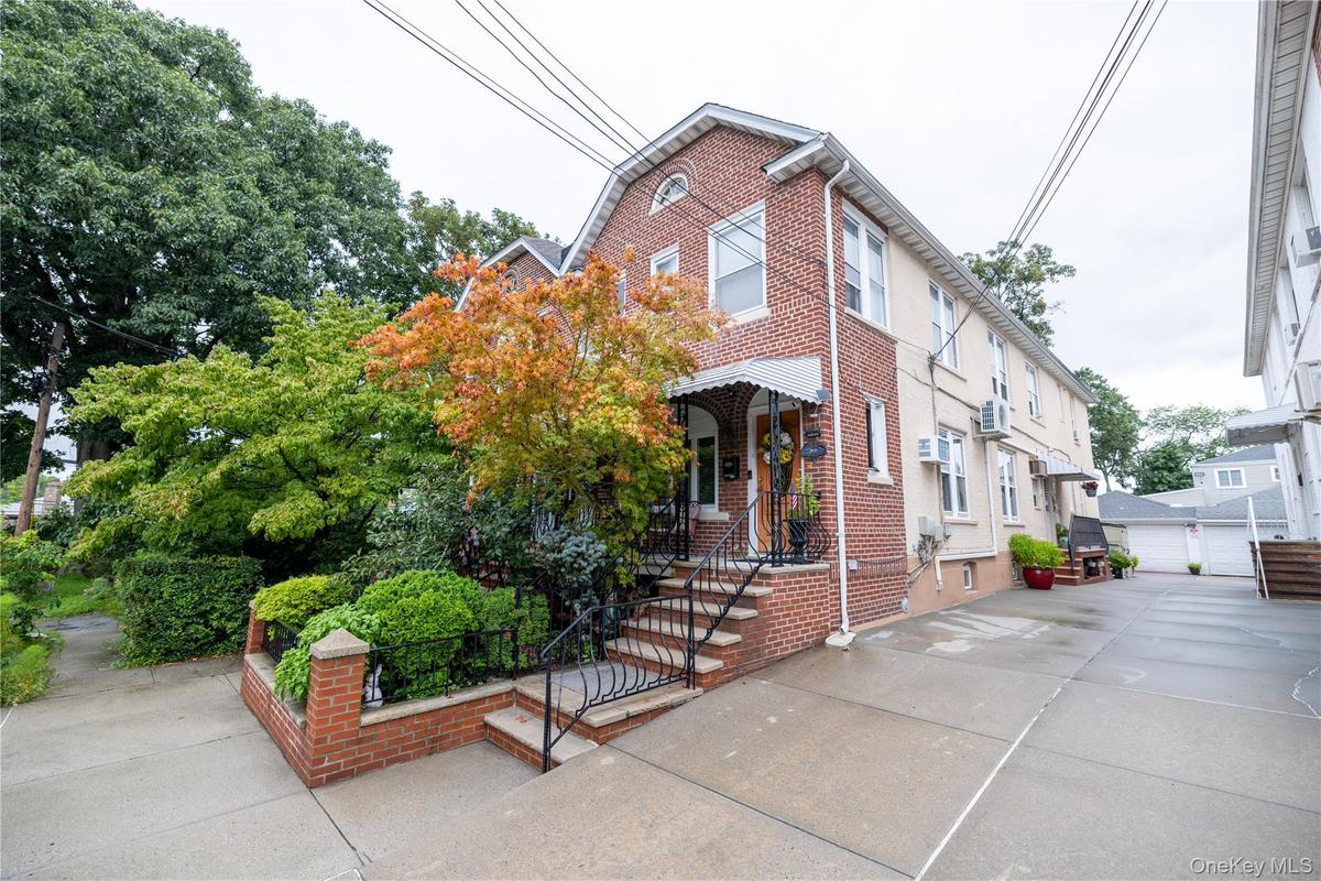 Brick and stucco exterior with multiple windows, a concrete driveway, and mature landscaping