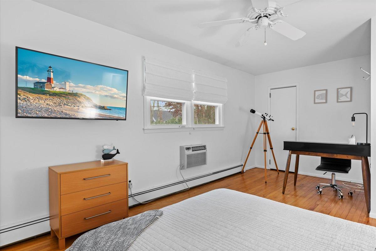 Bedroom with baseboard heating, a baseboard radiator, an AC wall unit, a ceiling fan, and wood finished floors