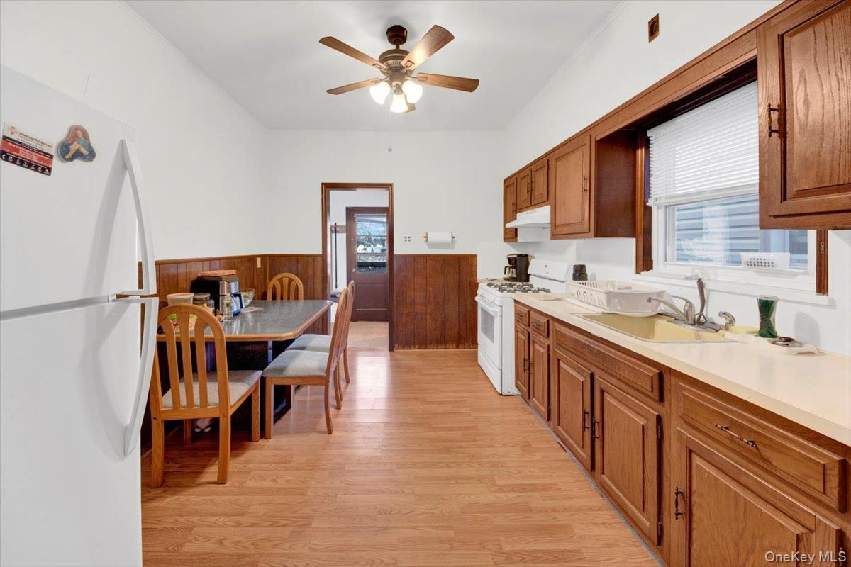 Kitchen featuring white appliances, brown cabinets, light countertops, light wood-type flooring, and a wainscoted wall
