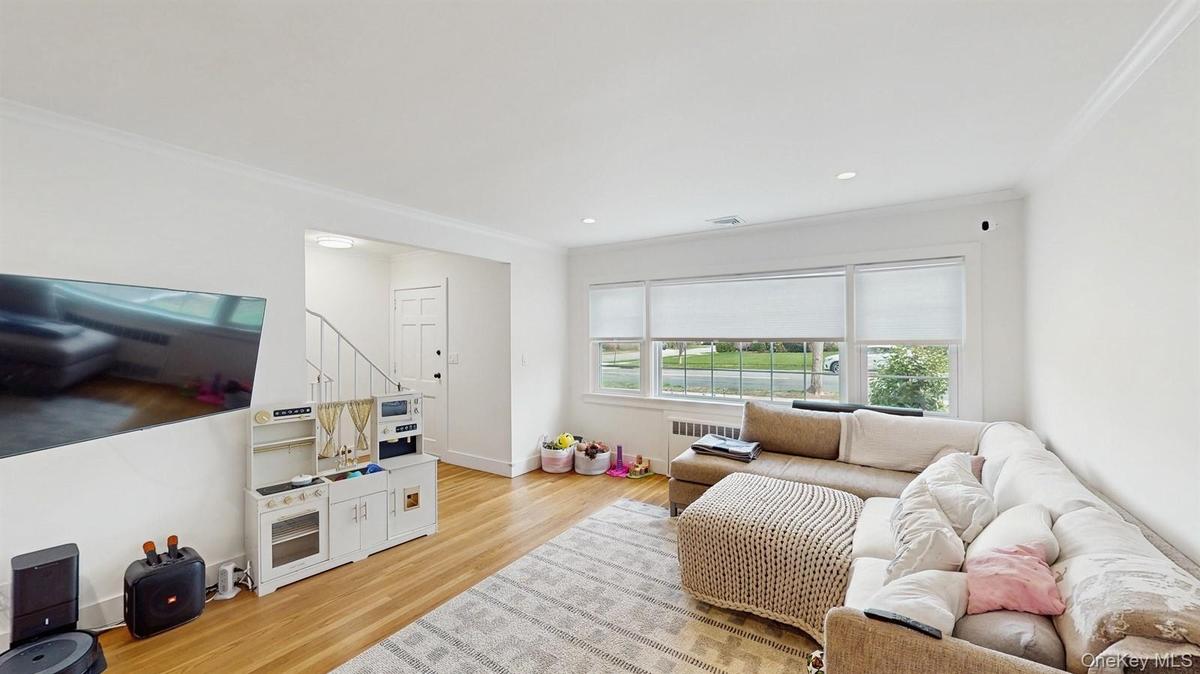 Living room featuring baseboards, ornamental molding, light wood-style floors, recessed lighting, and radiator