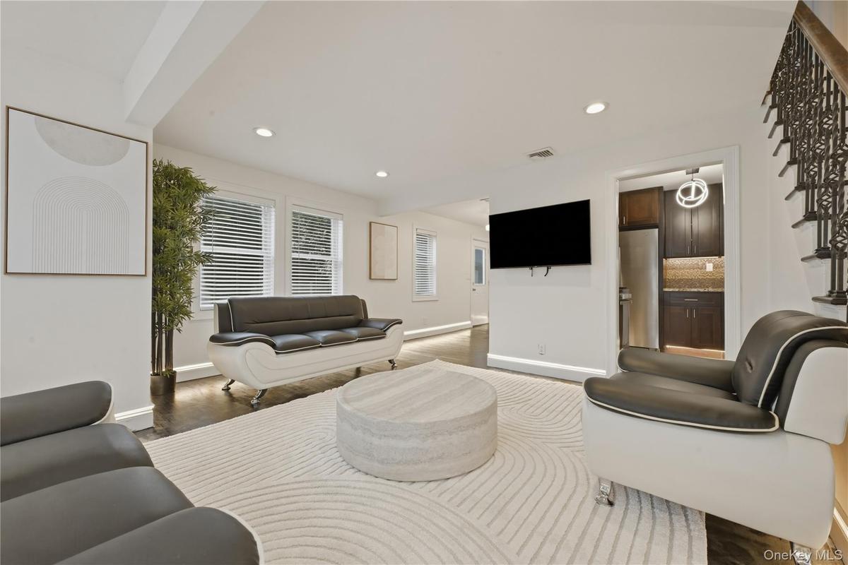Spacious living area featuring dark wood-finish flooring, recessed lighting, and white walls